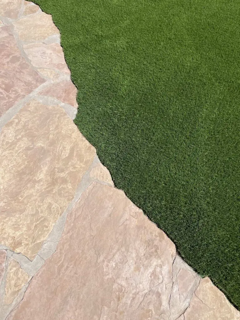 Natural stone pavers laid next to artificial grass. Showing intricate edging detail