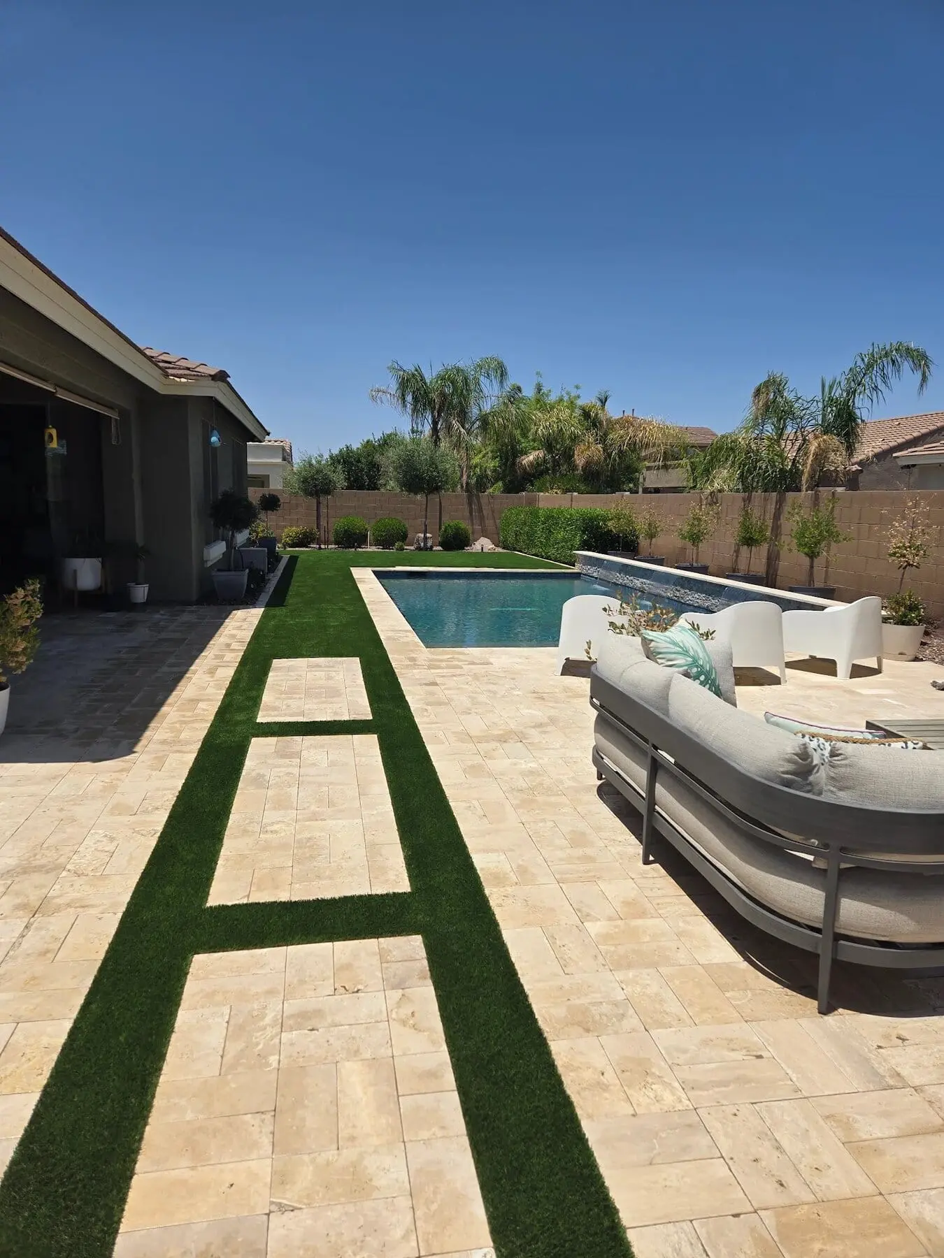 artificial grass and travertine pavers installed next to a pool deck in Chandler az