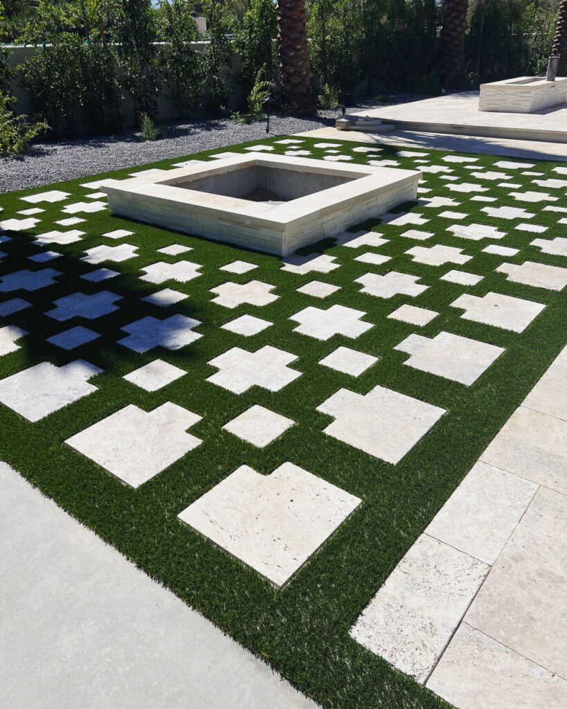 Custom cut travertine pavers in a light color, laid into artificial turf, surrounding a travertine fire pit