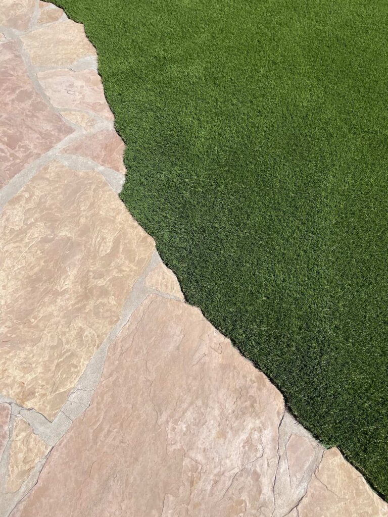 Natural stone pavers laid next to artificial grass. Showing intricate edging detail