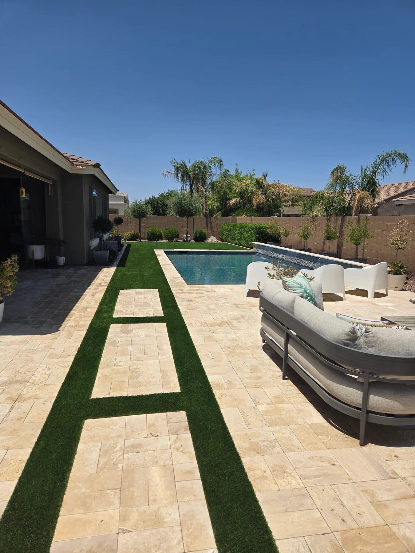 artificial grass and travertine pavers installed next to a pool deck in Chandler az