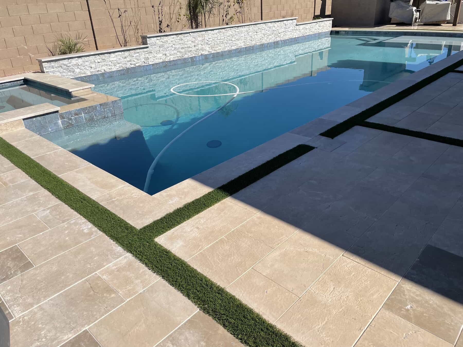 Travertine pavers with artificial grass strips in between installed by a turf company called Apex Turf 