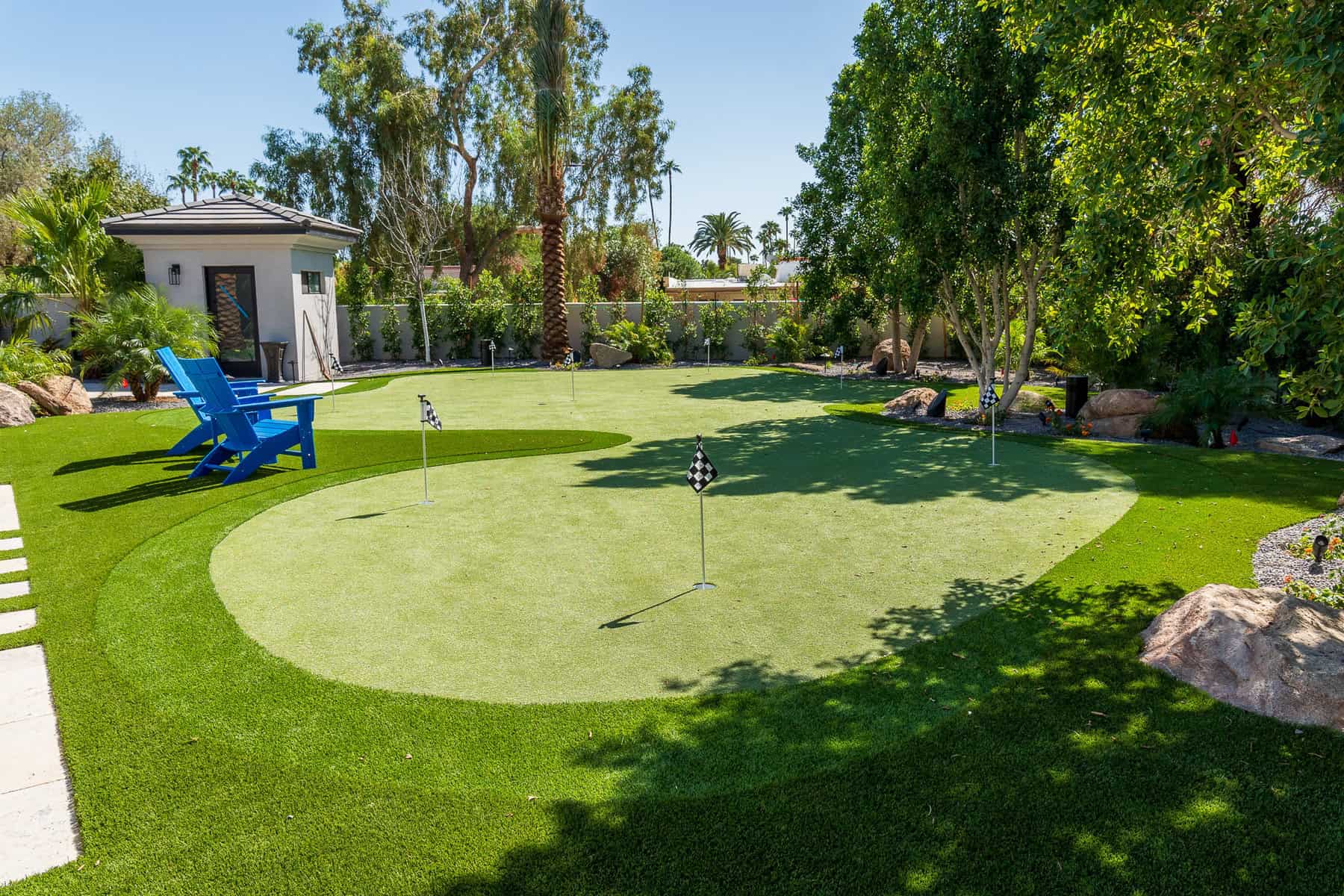 A white dog with one floppy ear and one upright ear is lounging on vibrant pet turf, facing forward and smiling. Its tail is relaxed, and the artificial grass beneath looks freshly cut and lush.
