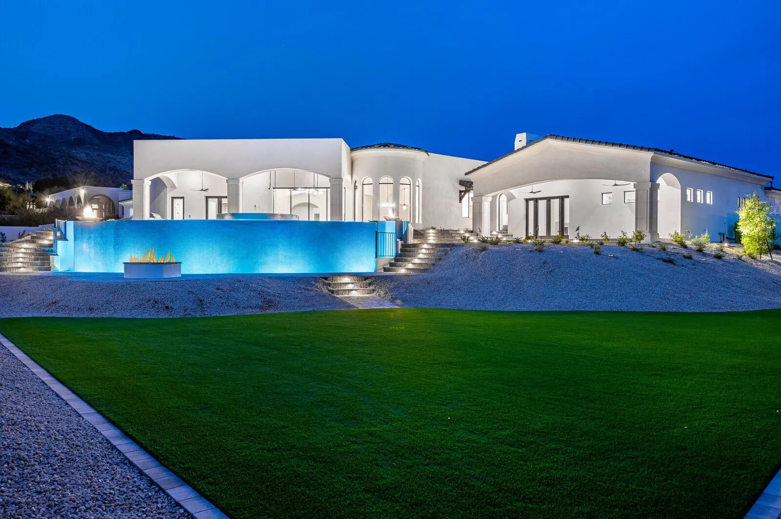 Night time photo of a large luxurxy home in Chandler Arizona with LED landscape lighting illuminating the stairs, pool and garden plants. All installed by Apex Turf in Chandler
