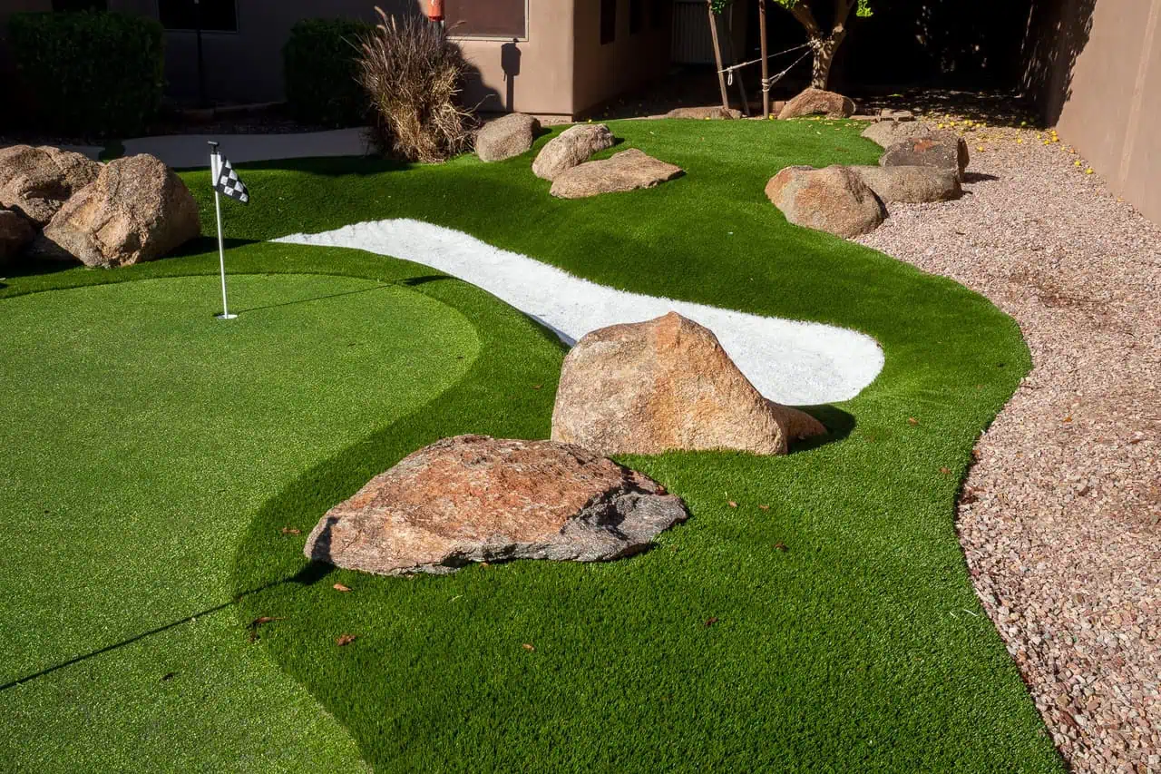 artificial turf putting green at a home in Fountain Hills Arizona. There is a synthetic bunker with boulders as a feature and 1 hole and flag showing