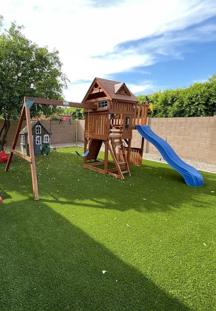 Artificial grass for playgrounds laid in a backyard in Phoenix Arizona. Picture shows a playhouse with a slide and two swings