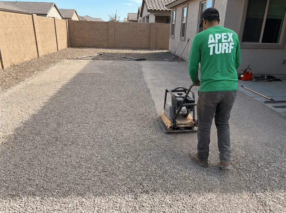 Apex Turf crew member in a residential yard in Phoenix using a plate compactor to compact down crushed granite or quarter minus stone in preparation to lay synthetic grass.