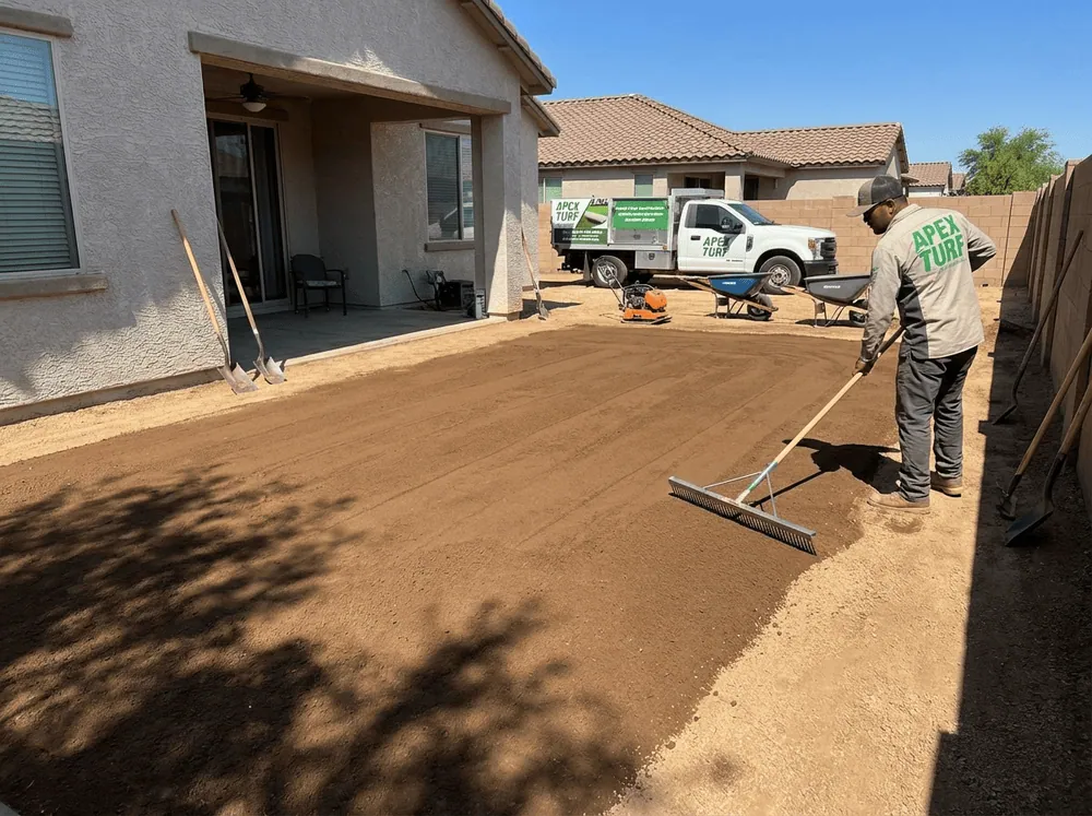 An Apex Turf crew member in a residential backyard in Phoenix Arizona, raking the soil, getting ready to lay and compact quarter minus rock for an artificial turf installation