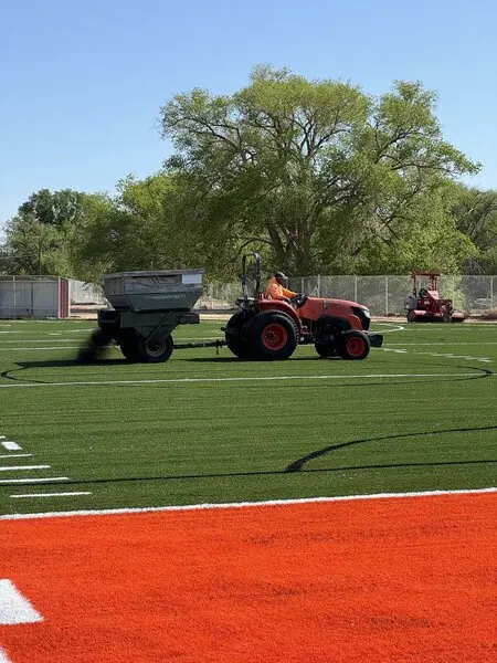 Infill spreader being towed behind a tractor, spreading the sports infill over a newly installed football field