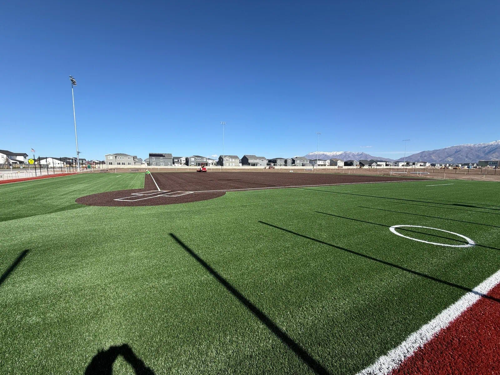 An astoturf softball field with green turf outfield and brown turf infield. Large amongst a residential setting in Arizona