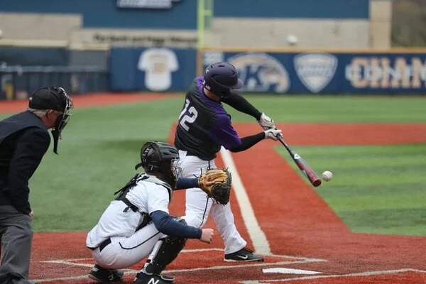 Baseball player making contact with a ball in the batters box. Catcher behind him with his glove outstretched. Playing at a baseball facility in Arizona