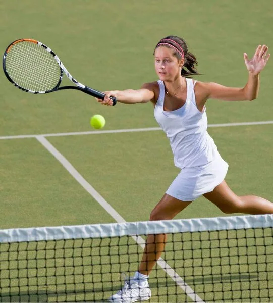 A female tennis player running has just returned a volley over the net on an astroturf court